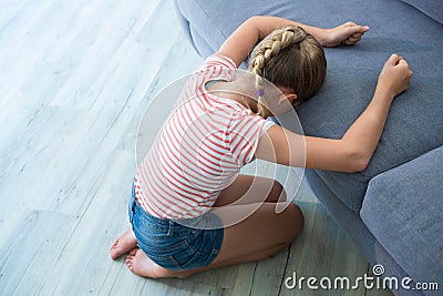 Sad girl kneeling by sofa at home Stock Photo