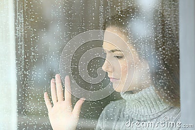 Sad girl looking through a window in a rainy day Stock Photo