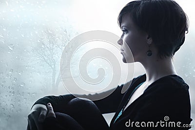 Sad girl on the windowsill looking out window Stock Photo