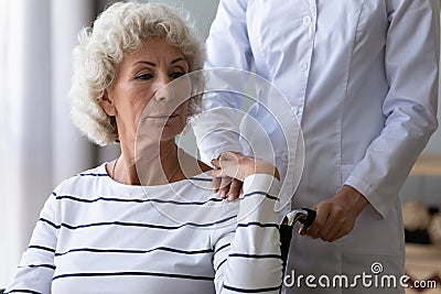 Sad handicapped woman sitting in wheelchair holding hand of caregiver Stock Photo