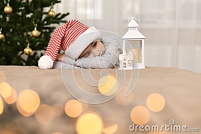 Sad kid in a striped cap lies at the Christmas tree Stock Photo