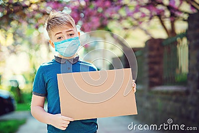 Sad kid wearing protective mask. Boy showing empty blank. Cute boy holding empty board outdoors. World global pandemic. Stock Photo