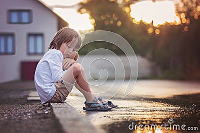 Sad little boy, sitting on the street in the rain, hugging his t Stock Photo