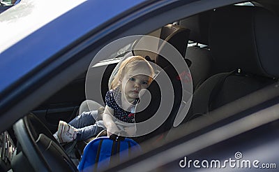 Sad little child girl alone in the car waiting for the parent strapped in a child car seat. It is dangerous to leave Stock Photo