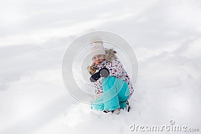 Sad little girl sitting in a snowy forest in the winter and crying, her clothes stained with snow Stock Photo