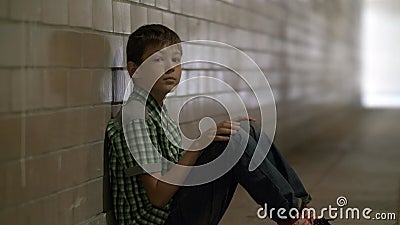 Sad lonely battered boy sits on the floor in a tunnel in deep depression looking at the camera, no one is waiting for Stock Photo