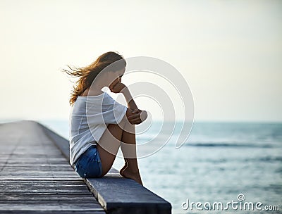 Sad lonely beautiful woman sitting on the pier Stock Photo