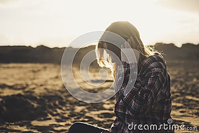 Sad lonely girl sit down at the beach during the dusk of the sunset - golden colors and sand in background for people love to be Stock Photo