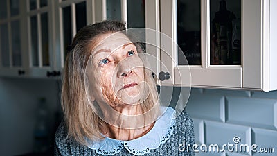 Sad lonely old gray haired woman looking through the window. Vulnerable person in quarantine Stock Photo
