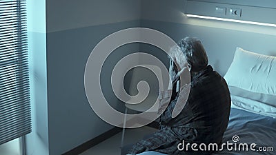 Sad lonely senior sitting in a hospital bed at night Stock Photo