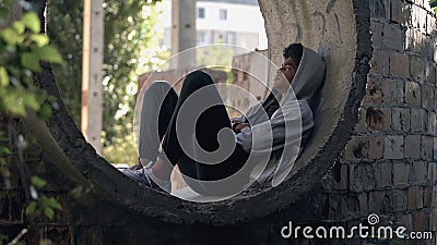 Sad lonely student in hoodie sitting alone abandoned building, puberty isolation Stock Photo