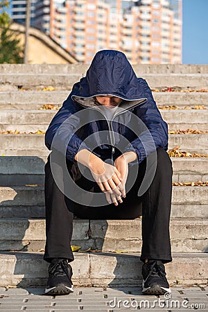 Sad lonely troubled teenage boy with hands down sitting on steps outdoors Stock Photo