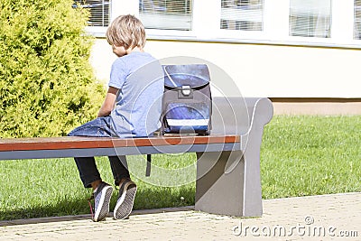 Sad, lonely, unhappy, disappointed boy sitting alone near school. Backpack. Casual clothes. Outdoor Stock Photo