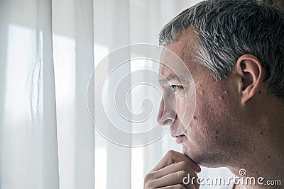 Sad man looking out the window. Feeling hopeless. Depressed mature man standing near the window Stock Photo