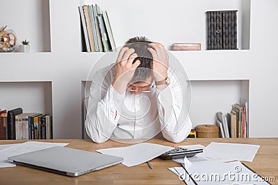 Sad manager getting notice of dismissal, sitting at workplace with laptop and financial documents, employee receiving letter with Stock Photo