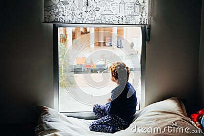 Sad and melancholic boy looks through a window in his apartment during his confinement Stock Photo