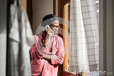 Sad upset African man having difficult conversation on phone, standing by window at home Stock Photo