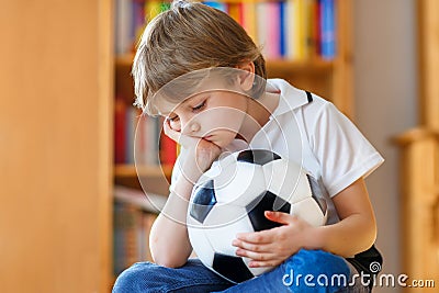 Sad and not happy little kid with football about lost football or soccer game. child after watching match on tv Stock Photo