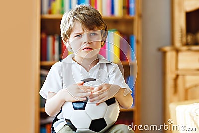 Sad and not happy little kid with football about lost football or soccer game. child after watching match on tv Stock Photo