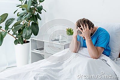 sad patient in medical gown touching head in hospital. Stock Photo