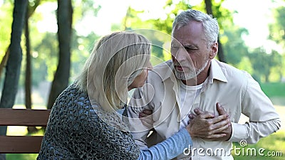 Sad retired man feeling heart pain, cardio problems, wife supporting husband Stock Photo