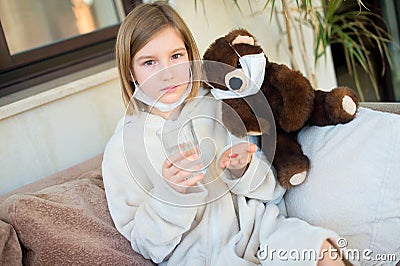 Sad sick toddler girl with fever in medicine mask ready to take cure pills and get well soon Stock Photo