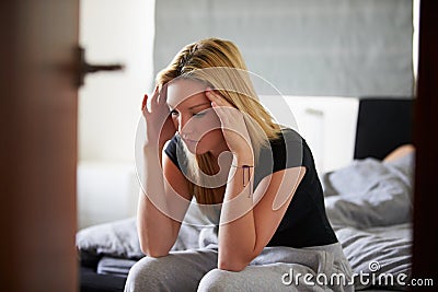 Sad Teenage Girl Sitting In Bedroom Whilst Boyfriend Sleeps Stock Photo