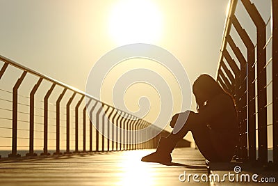 Sad teenager girl depressed sitting in a bridge at sunset Stock Photo