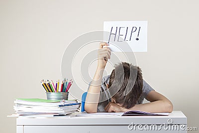 Sad tired frustrated boy sitting at the table with many books and holding paper with word Help. Learning difficulties Stock Photo