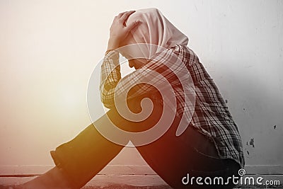 Sad unhappy lonely and depressed young Asian muslim woman crouching and crying at home. Stress exhausted feeling down expression Stock Photo