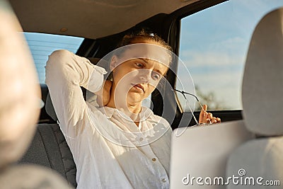 Sad unhappy tired woman wearing white shirt in automobile working online on laptop massaging neck feeling exhausted looking at Stock Photo