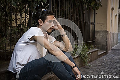 Sad, unhappy young man outdoor, sitting on pavement Stock Photo