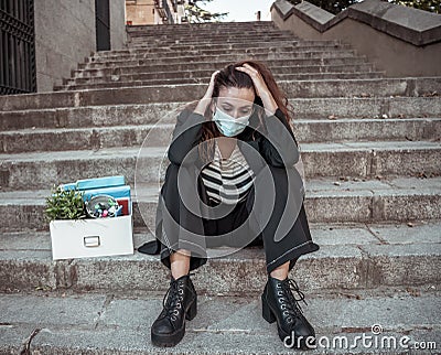 Sad woman in face mask with office box feeling hopeless after losing job due to coronavirus job cuts Stock Photo