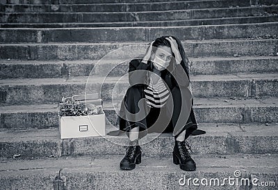 Sad woman in face mask with office box feeling hopeless after losing job due to coronavirus job cuts Stock Photo