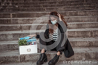 Sad woman in face mask with office box feeling hopeless after losing job due to coronavirus job cuts Stock Photo
