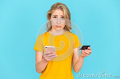 Sad woman looking at camera, holding smartphone and plastic card in hands Stock Photo