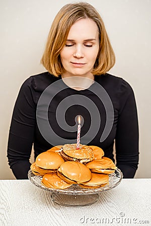 a sad woman makes a wish and blows out a candle on a hamburger cake. Stock Photo