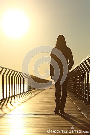 Sad woman silhouette walking alone at sunset Stock Photo