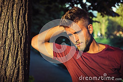 Sad, worried blond young man against tree Stock Photo