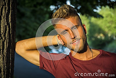 Sad, worried blond young man against tree Stock Photo