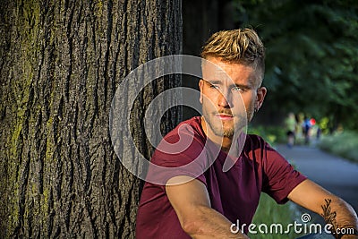 Sad, worried blond young man against tree Stock Photo