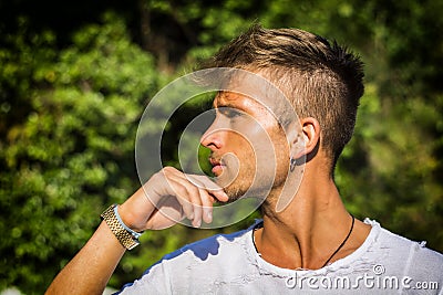 Sad, worried blond young man against trees Stock Photo