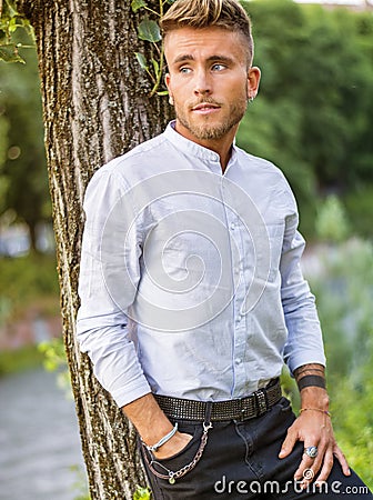 Sad, worried blond young man against tree Stock Photo
