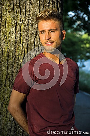 Sad, worried blond young man against tree Stock Photo