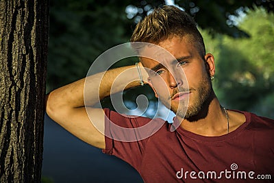 Sad, worried blond young man against tree Stock Photo