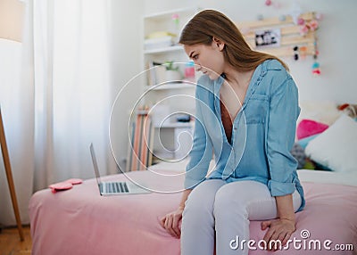 Sad and worried young girl with laptop sitting indoors, internet abuse concept. Stock Photo