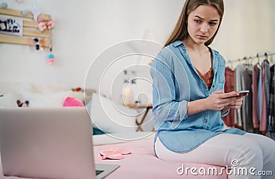 Sad and worried young girl with laptop sitting indoors, internet abuse concept. Stock Photo