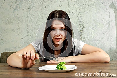 Sad young brunette woman dealing with anorexia nervosa or bulimia having small green vegetable on plate. Dieting problems, eating Stock Photo