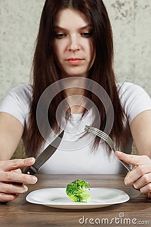 Sad young brunette woman dealing with anorexia nervosa or bulimia having small green vegetable on plate. Dieting problems, eating Stock Photo