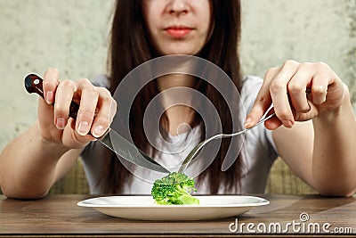 Sad young brunette woman dealing with anorexia nervosa or bulimia having small green vegetable on plate. Dieting problems, eating Stock Photo